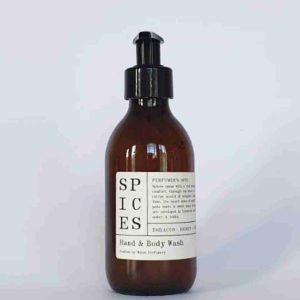 an amber glass bottle with a black pump lid, and a cream paper label. the label says that this is scented hand and body wash in spices scent made by Wales Perfumery