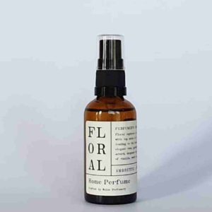 an amber glass bottle with a black spray pump lid, and a cream paper label. the label says that this is home perfume spray in floral scent made by Wales Perfumery