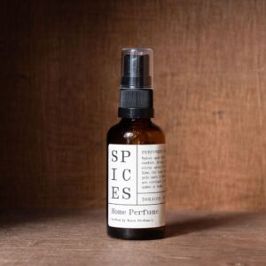 Amber glass spray bottle labelled "Spices Home Perfume" by Wales Perfumery, standing against a brown wood backdrop.