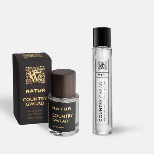 A Wales Perfumery Natur Country Gwlad 30ml Eau de Parfum in a clear glass bottle with a dark wooden cap, alongside its black and gold gift box, and a slim Country Gwlad Mist featuring neroli, freshly cut grass and fig leaf, on a light grey background.