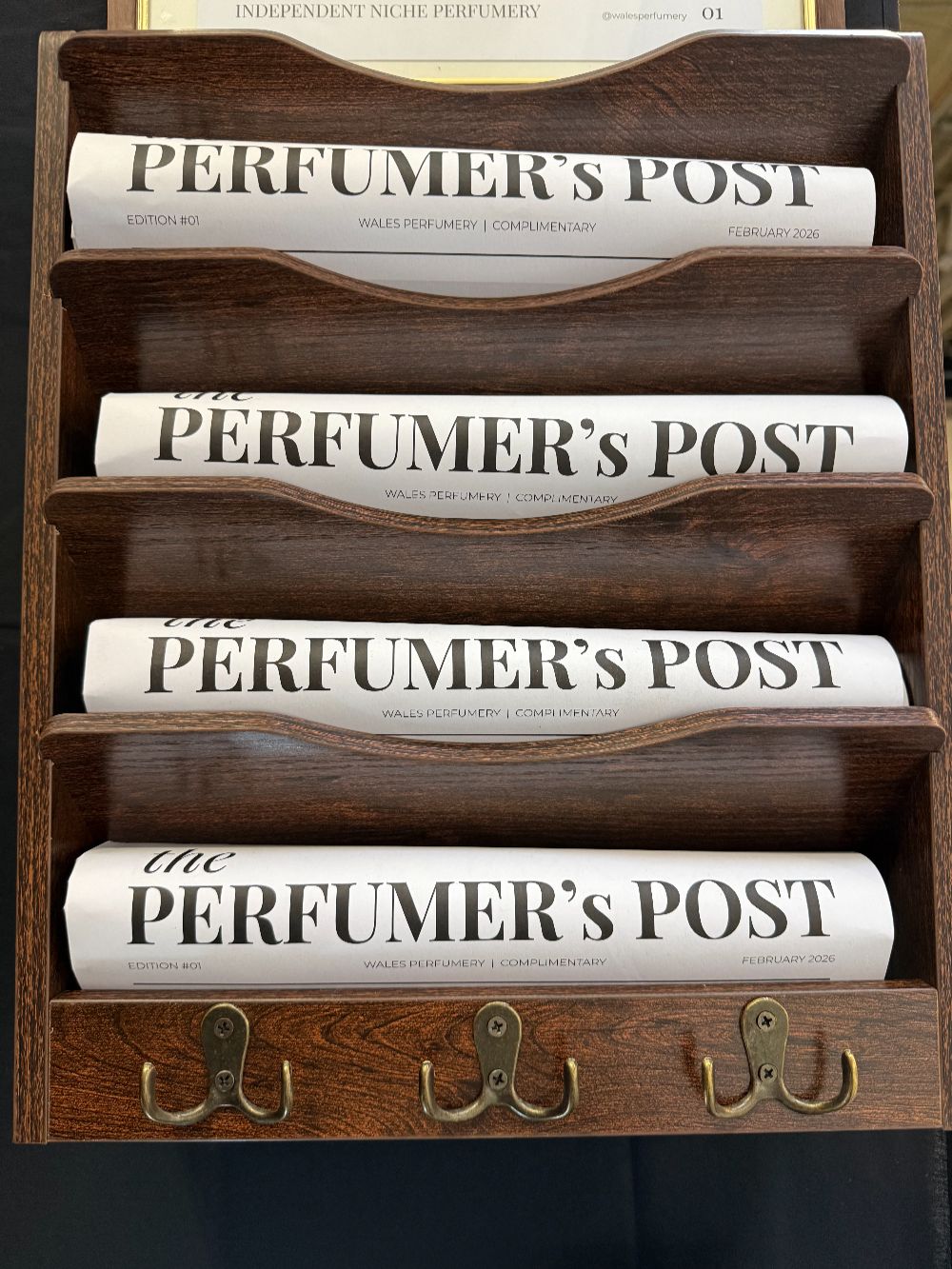 a vintage dark wood newspaper rack with a paper called the perfumer's post visible